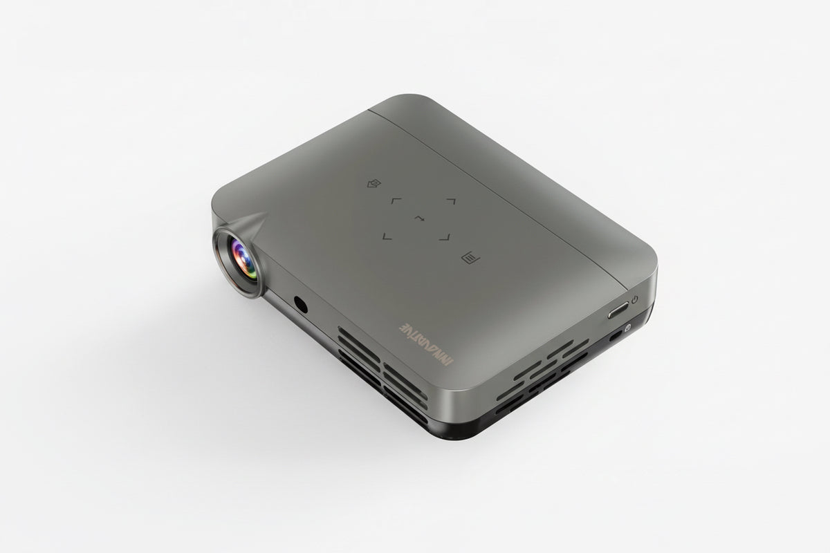 A compact and portable projector with a visible lens on the front, along with ports and controls. The projector appears to be gray in color.