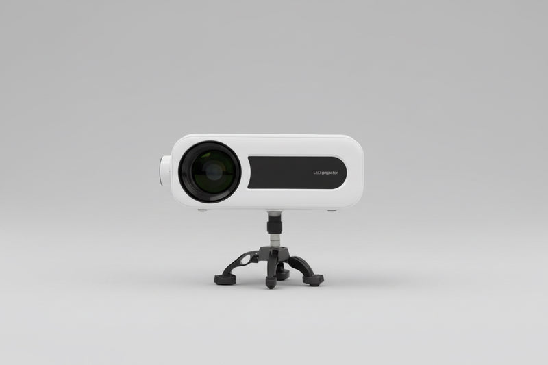 A white MINIO Elite HDMI projector placed on a stand outdoors, with a clear lens visible and a blurred background.